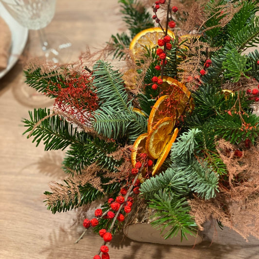 centre de table buche fleurie decoree avec du sapin et des oranges sechees