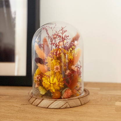 globe fleuri fleurs sechees tons orange et jaune sur un socle en bois avec un globe en verre