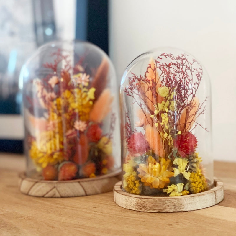 globe fleuri fleurs sechees tons orange et jaune sur un socle en bois avec un globe en verre